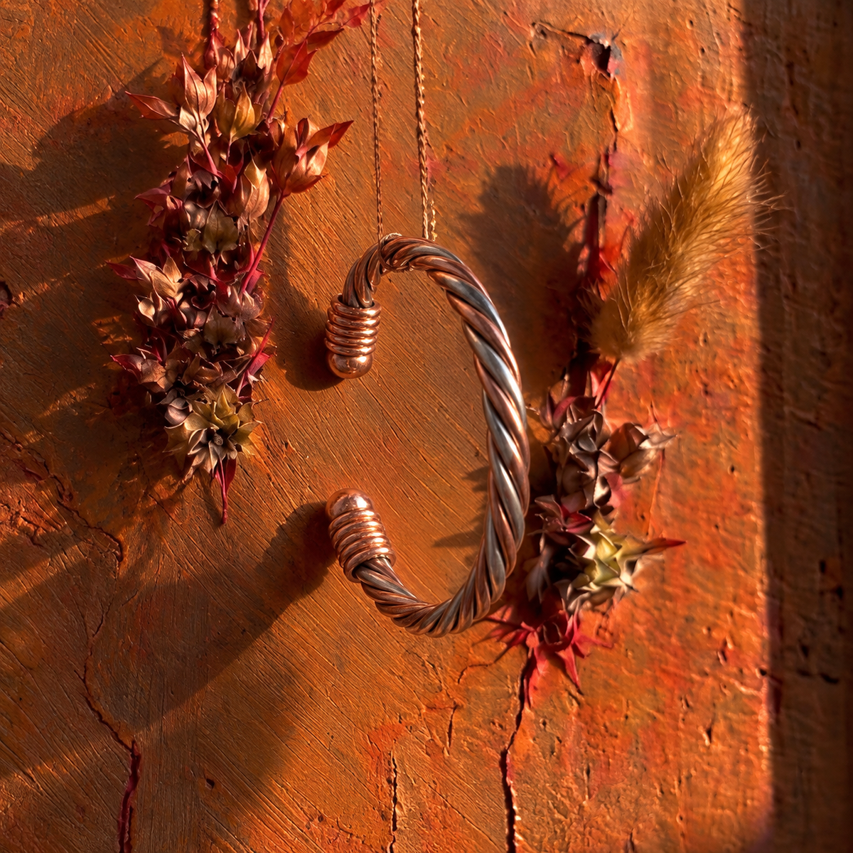 Cuivre Ondine twisted copper cuff bracelet hanging against a terracotta wall with dried flowers